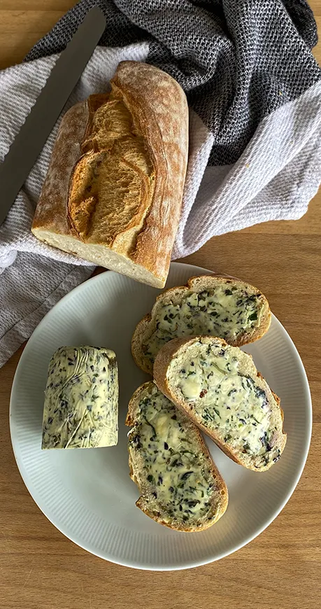 Baguette auf 2 Tellern mit Microgreens Kräuterbutter bestrichen und einem Messer